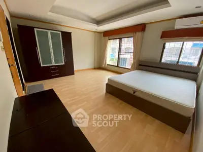 Spacious bedroom with large windows and wooden flooring in modern apartment.