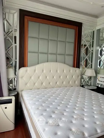 Luxurious bedroom with elegant headboard and plush mattress, featuring mirrored accents and stylish lamps.