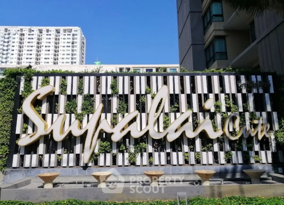 Modern building facade with Supalai signage and lush greenery, showcasing urban living elegance.