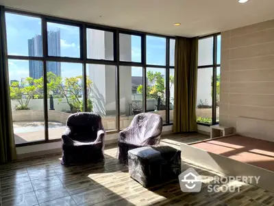 Spacious living room with large windows offering abundant natural light and a serene view, complemented by a cozy balcony area.