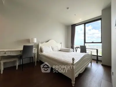 Spacious bedroom with elegant white furniture and stunning city view from large window.