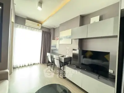 Modern living room with sleek furniture and large TV, featuring a stylish desk and ample natural light.
