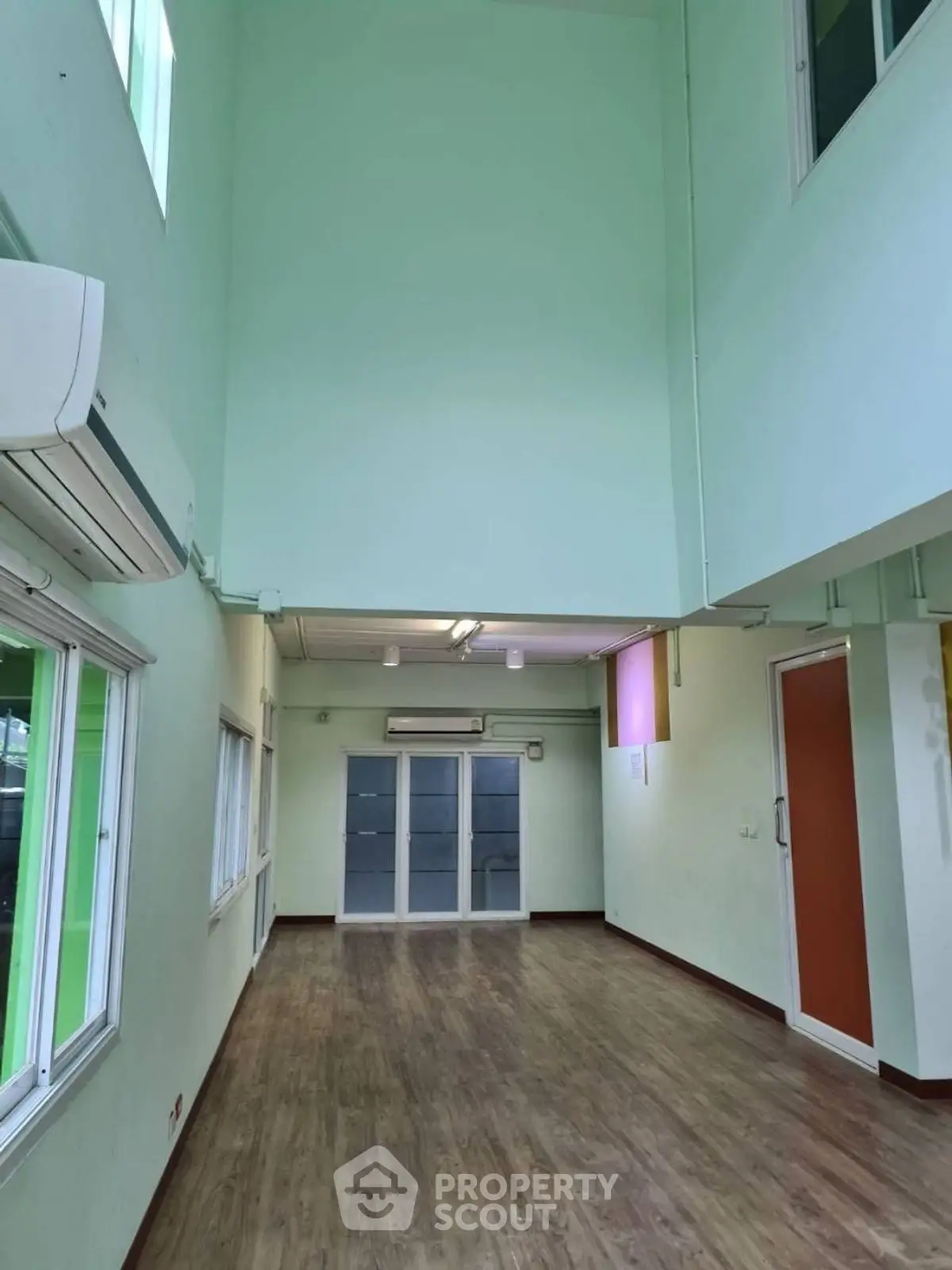 Spacious high-ceiling room with wooden flooring and large windows