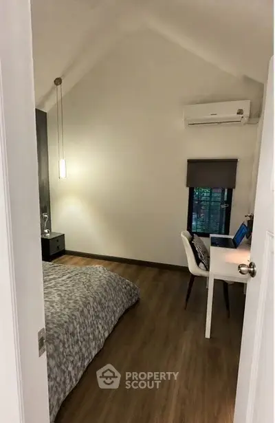 Cozy bedroom with modern decor and workspace, featuring wooden flooring and a stylish pendant light.