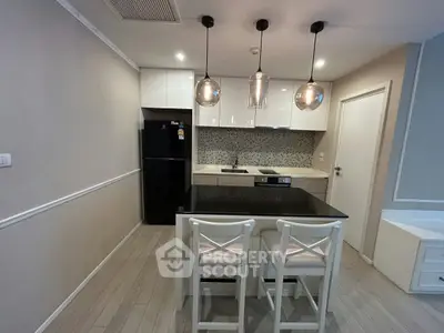 Modern kitchen with sleek design, featuring a black countertop, pendant lights, and white cabinetry.
