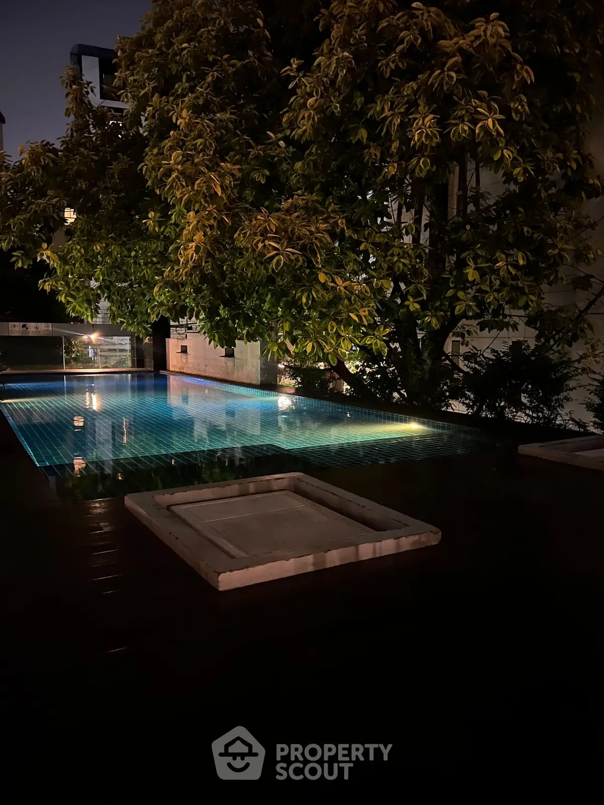 Luxurious night view of illuminated pool surrounded by lush greenery, perfect for serene relaxation.