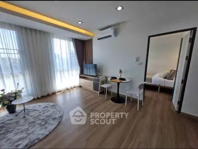 Modern living room with wooden flooring, cozy seating, and natural light, adjacent to a stylish bedroom.