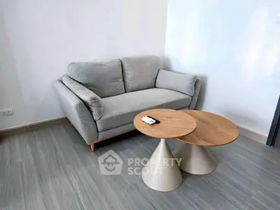 Modern living room with stylish gray sofa and unique wooden coffee tables on sleek flooring.