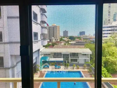 Stunning city view from apartment window overlooking a sparkling pool and urban skyline.