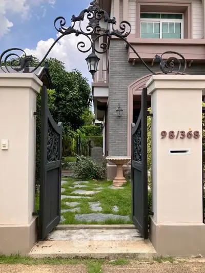 Charming entrance to a modern home with ornate gate and lush garden pathway.