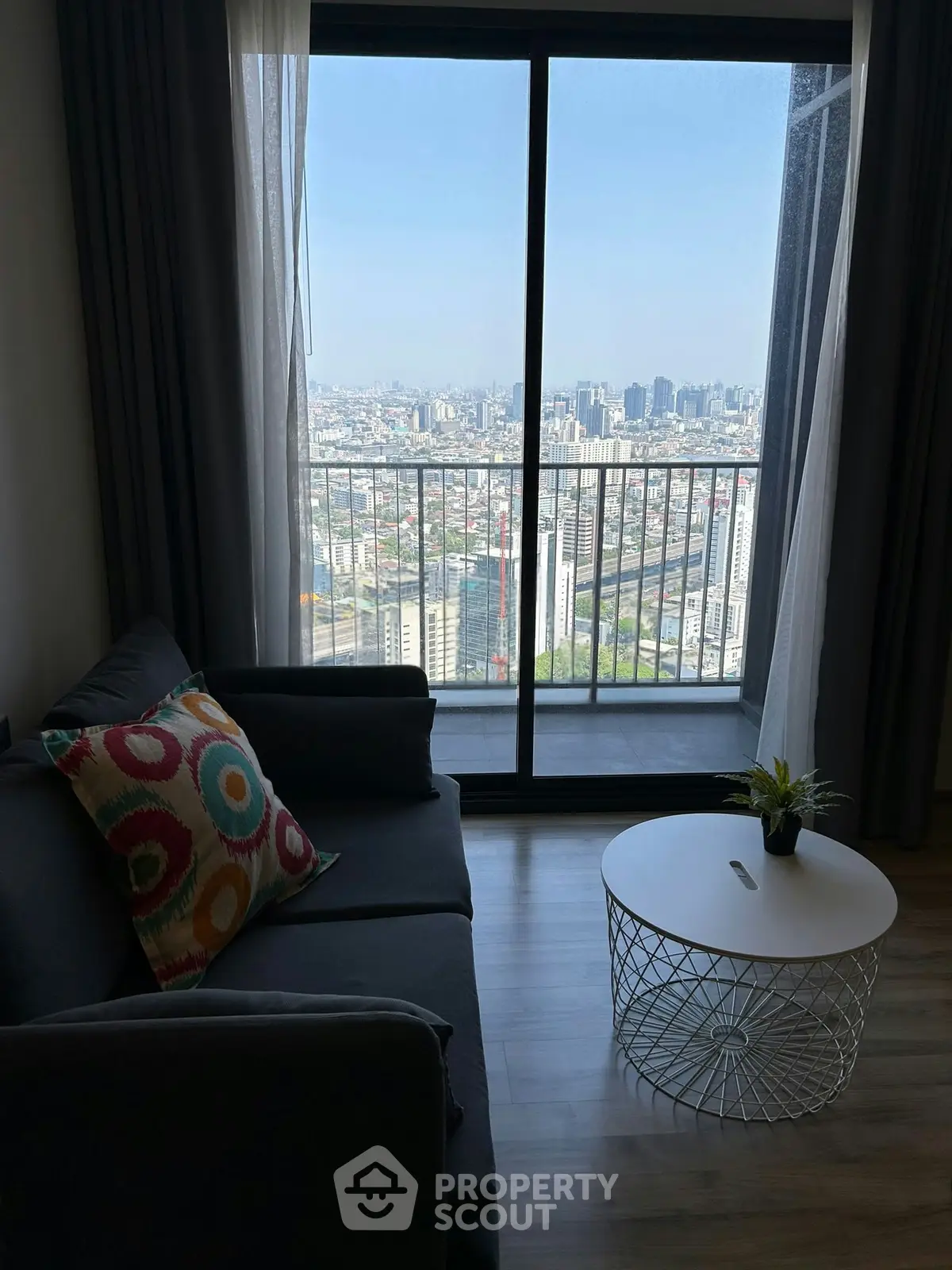 Stylish living room with stunning city view from high-rise balcony, featuring modern sofa and chic coffee table.