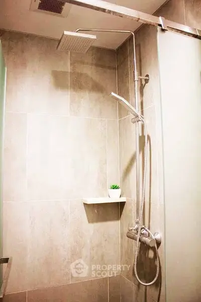 Modern bathroom shower with sleek design and neutral tiles, featuring a rainfall showerhead and small plant decor.