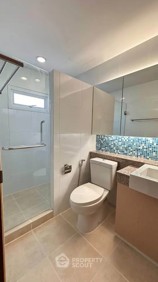 Modern bathroom with sleek design, featuring a glass shower enclosure and stylish mosaic tiles.
