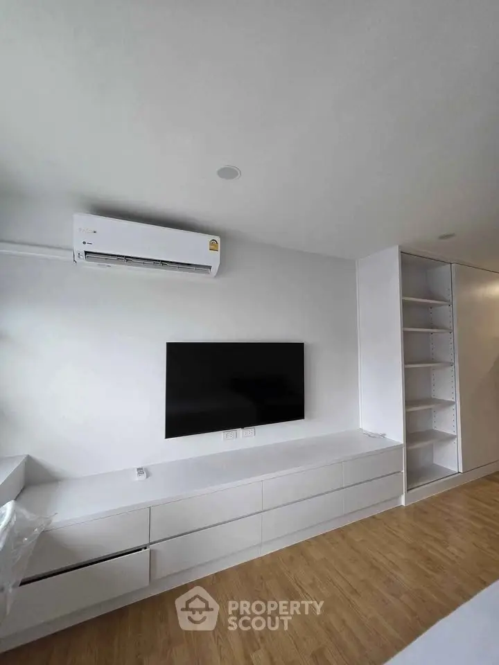 Modern living room with sleek white cabinetry and wall-mounted TV, featuring minimalist design and wooden flooring.