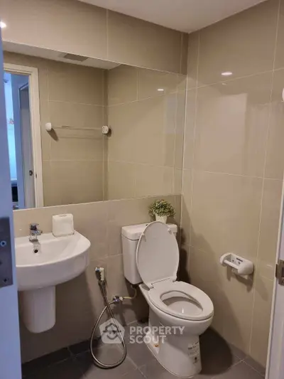 Modern bathroom with sleek fixtures and neutral tiles, featuring a toilet and sink.