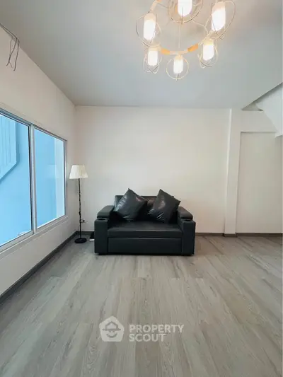 Modern living room with sleek black sofa and elegant lighting, featuring large window and stylish flooring.
