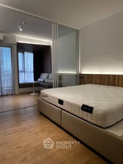 Modern bedroom with wooden flooring and cozy seating area near window.