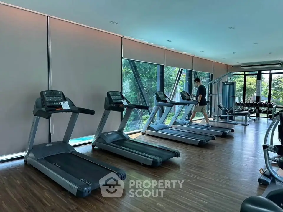 Modern gym with treadmills and large windows offering lush garden views.