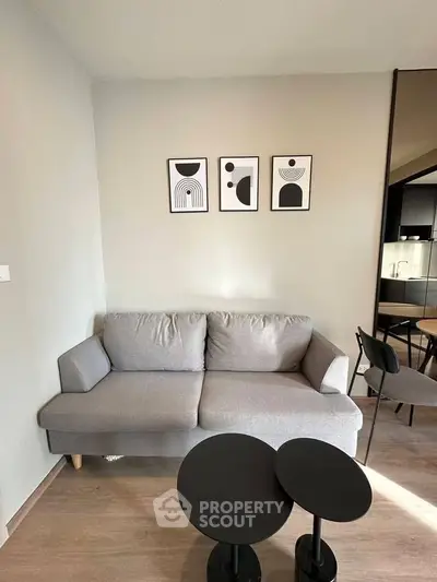 Modern living room with stylish gray sofa and abstract wall art, featuring sleek black tables and open kitchen view.