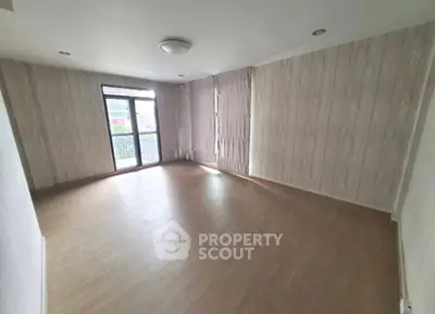 Spacious empty living room with wooden flooring and large window for natural light.