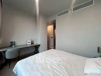 Modern bedroom with minimalist decor and study area, featuring neutral tones and ample natural light.
