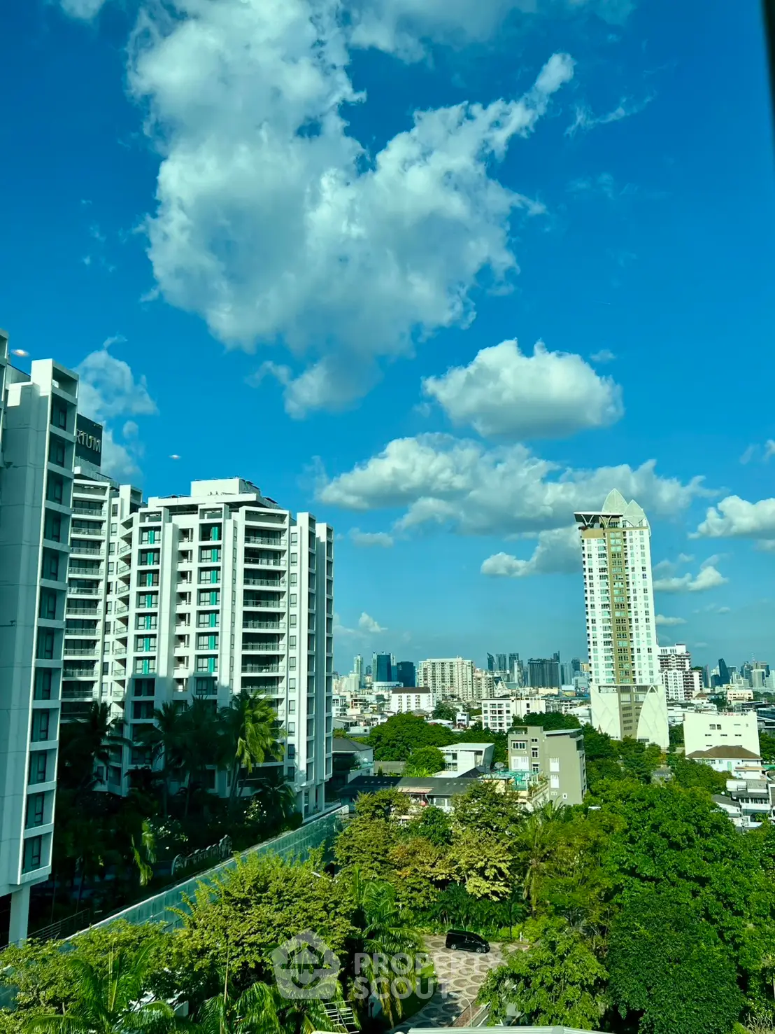 Stunning cityscape view with modern high-rise buildings and lush greenery under a vibrant blue sky.
