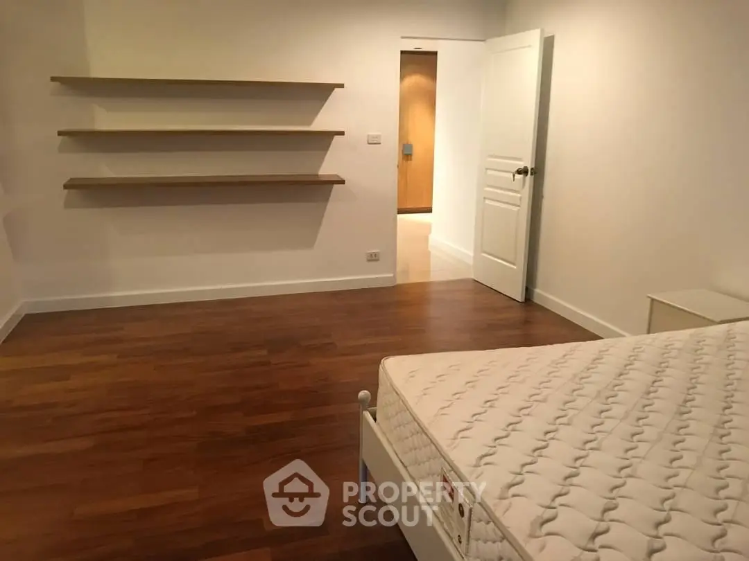 Spacious bedroom with wooden floors and minimalist design, featuring open shelves and a comfortable mattress.