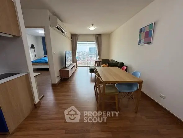 Modern open-plan living room with dining area and city view, featuring wooden flooring and stylish furniture.