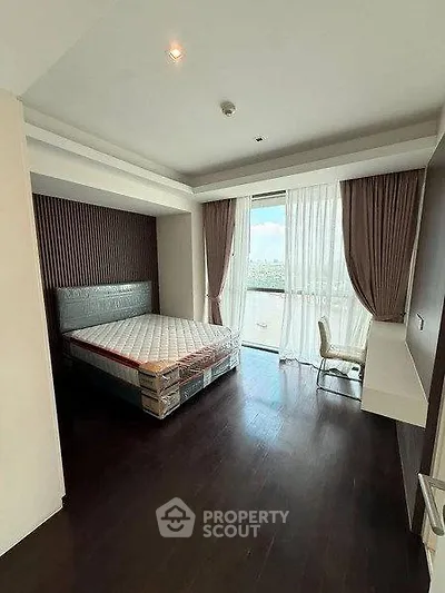 Spacious bedroom with large window and modern furnishings in a high-rise apartment.