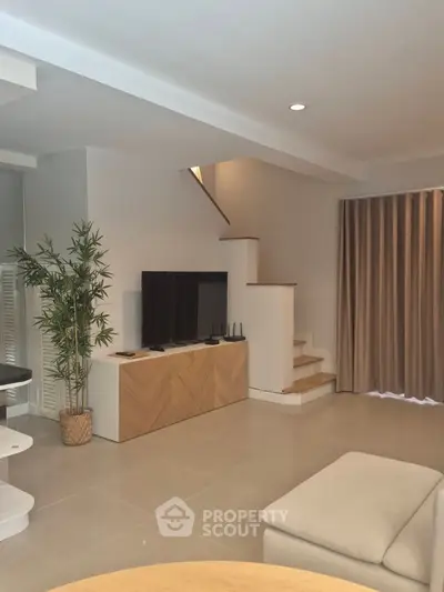 Modern living room with stylish decor and staircase, featuring a TV and elegant furniture.