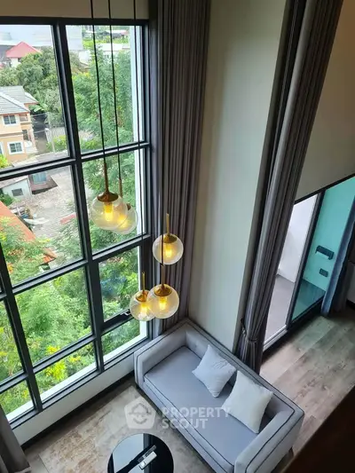 Stunning high-ceiling living room with large windows and modern decor, offering a serene view of lush greenery.