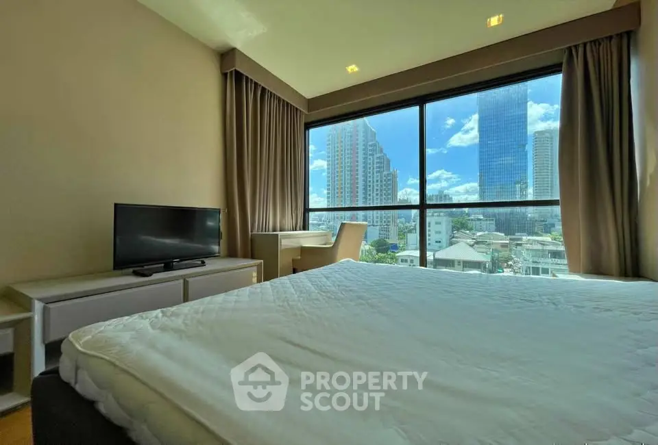 Spacious bedroom with large window offering stunning city views, modern furnishings, and natural light.
