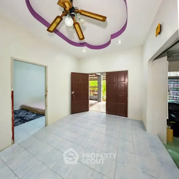 Spacious living room with unique ceiling design and fan, leading to a cozy bedroom and outdoor area.