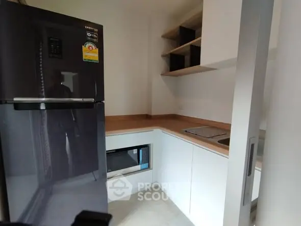 Modern kitchen with sleek appliances and minimalist design, featuring a fridge and built-in microwave.