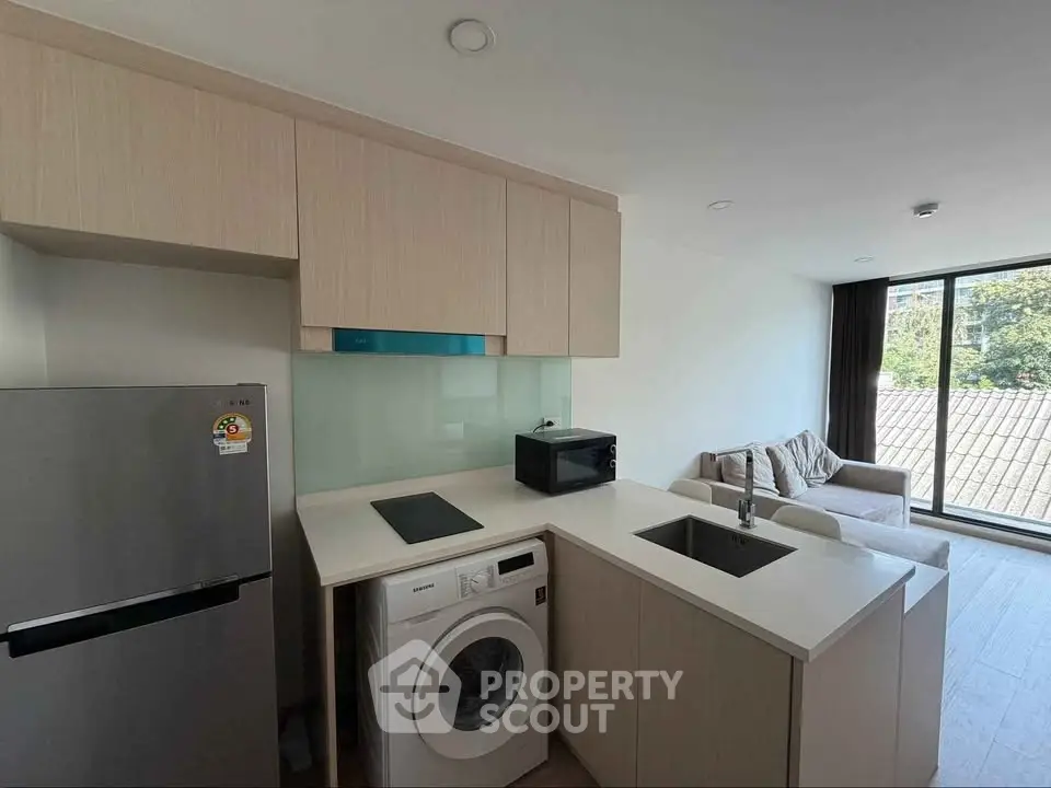 Modern kitchen with washing machine and cozy living area in open layout apartment.