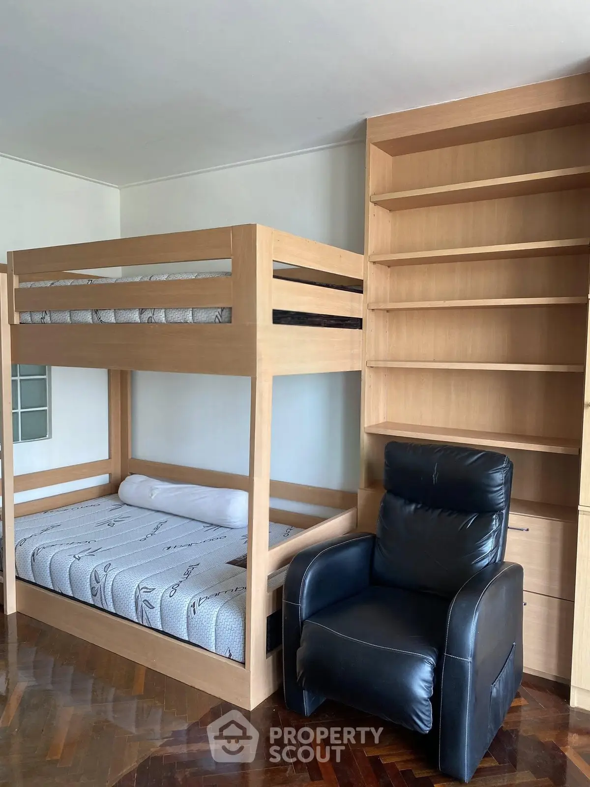 Spacious bedroom with bunk bed, leather armchair, and built-in wooden shelves.