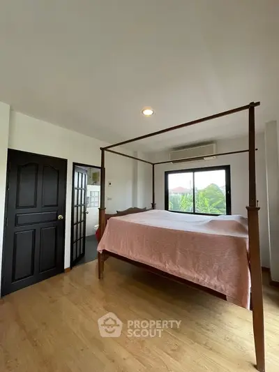 Spacious bedroom with elegant four-poster bed and large window view.
