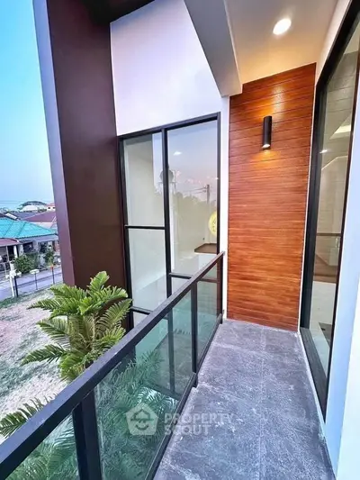 Modern balcony with sleek glass railing and wood paneling, offering a serene view of the neighborhood.