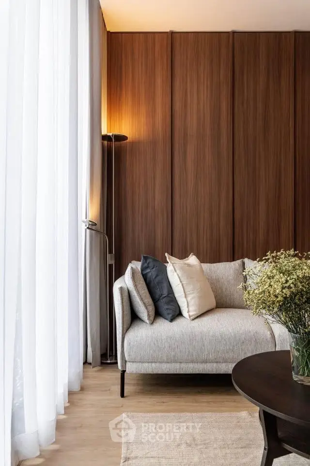 Elegant living room with modern sofa and floor lamp, featuring wooden panel wall and sheer curtains.