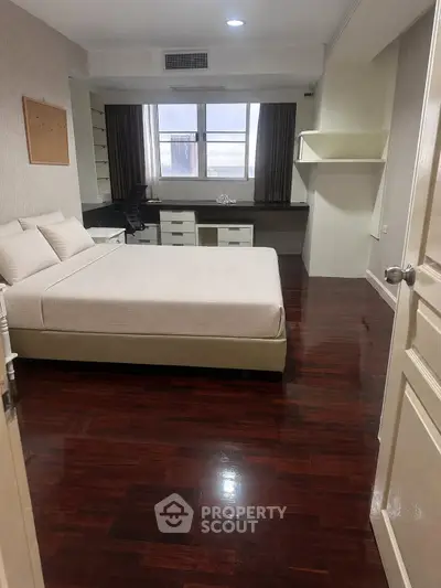 Spacious bedroom with polished wooden floors and modern furnishings in a well-lit apartment.