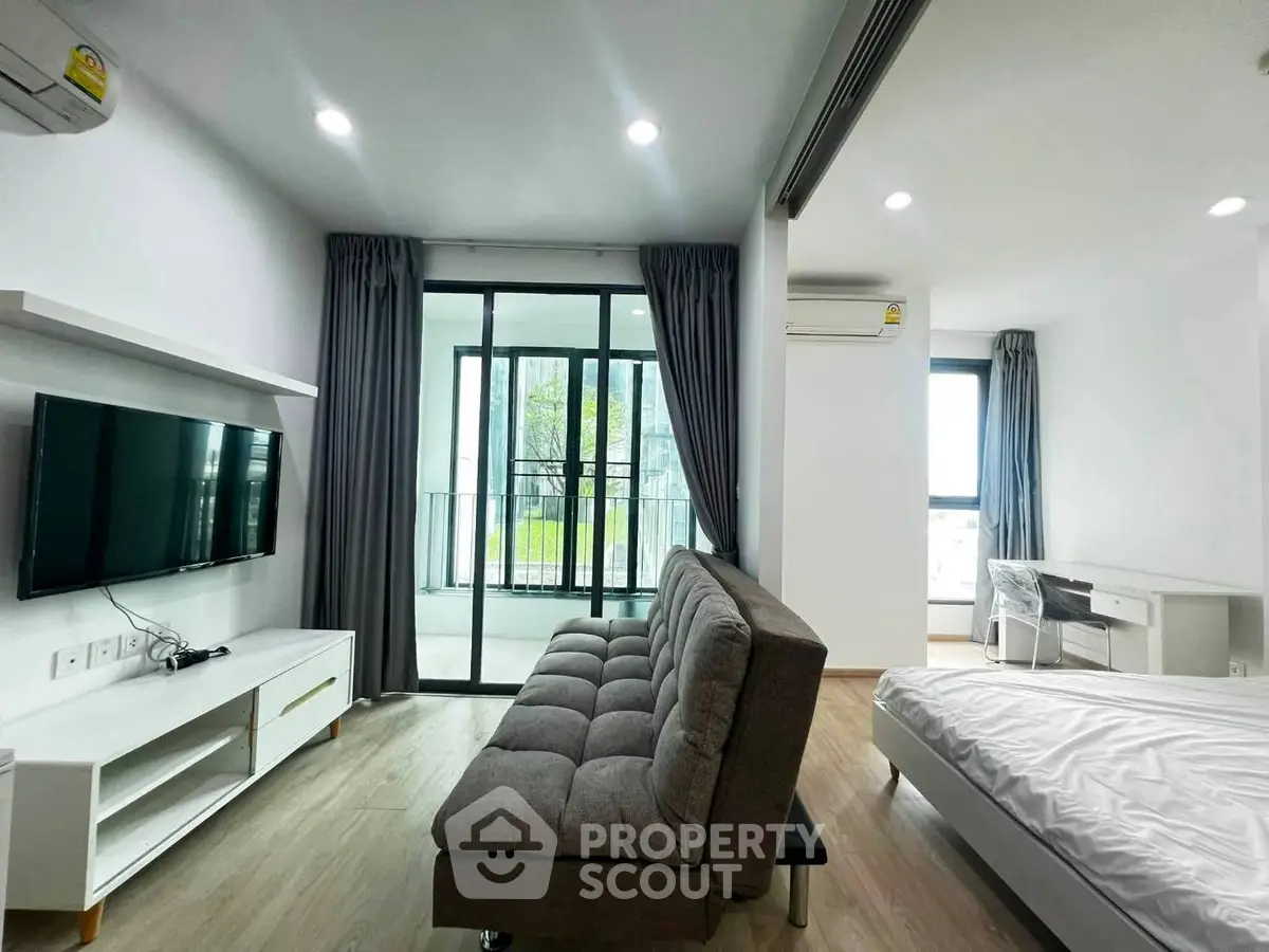 Modern studio apartment with balcony, featuring sleek furniture and abundant natural light.