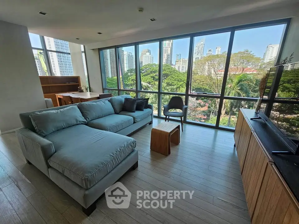 Spacious living room with large windows offering stunning city and park views, modern furniture, and natural light.