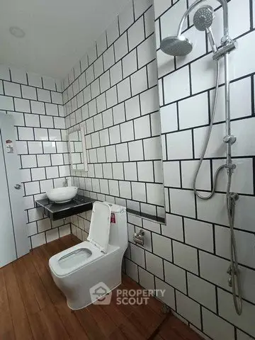 Modern bathroom with sleek white tiles and wooden flooring, featuring a stylish shower and contemporary fixtures.