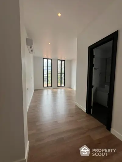 Spacious and bright living area with high ceilings, large windows offering natural light, and elegant wooden flooring, perfect for modern living.