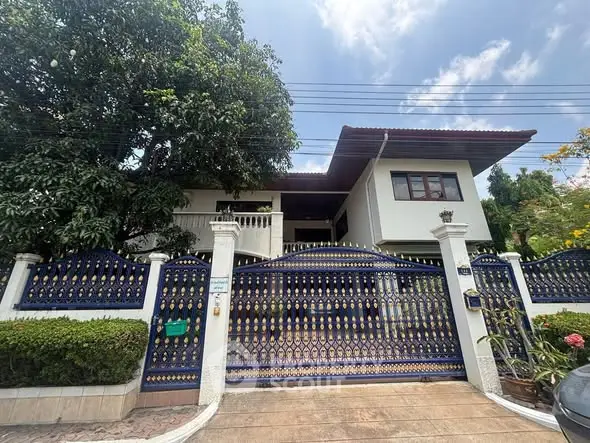 Charming two-story house with ornate gate and lush greenery, perfect for family living.