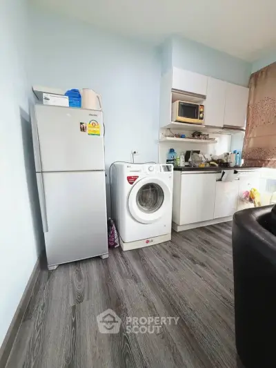 Compact kitchen with modern appliances including fridge and washing machine, featuring sleek flooring.