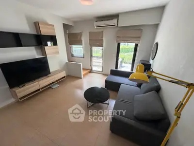 Modern living room with sleek furniture and large TV, featuring natural light and a cozy atmosphere.