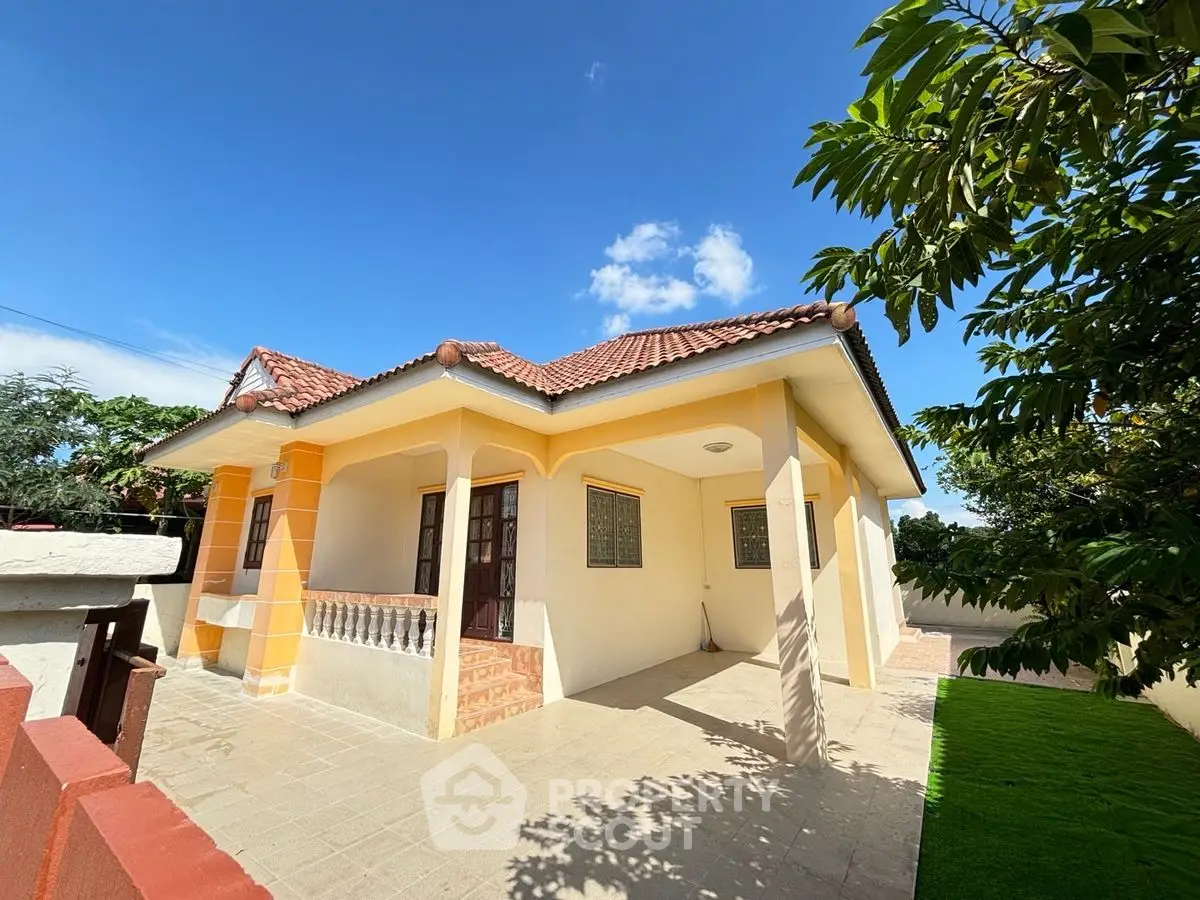 Charming single-story house with tiled roof and spacious front yard under clear blue sky.