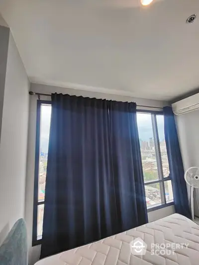 Modern bedroom with city view and large windows, featuring dark curtains and air conditioning.