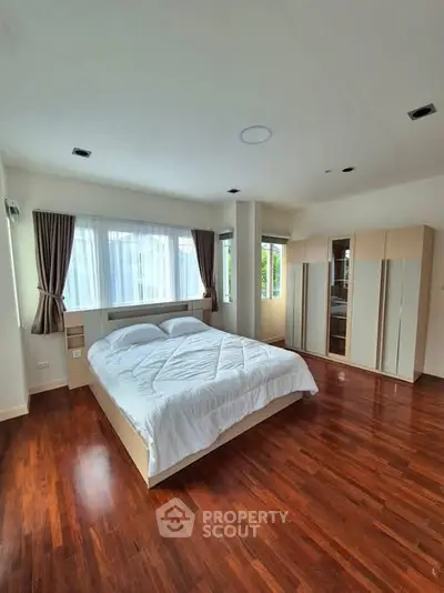 Spacious bedroom with wooden flooring and large windows in modern apartment